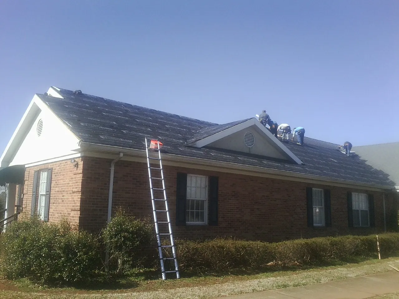 Crew tearing shingles off a brick ranch roof with a ladder set — Metal Roof Repair work by our crew in Bon Aqua