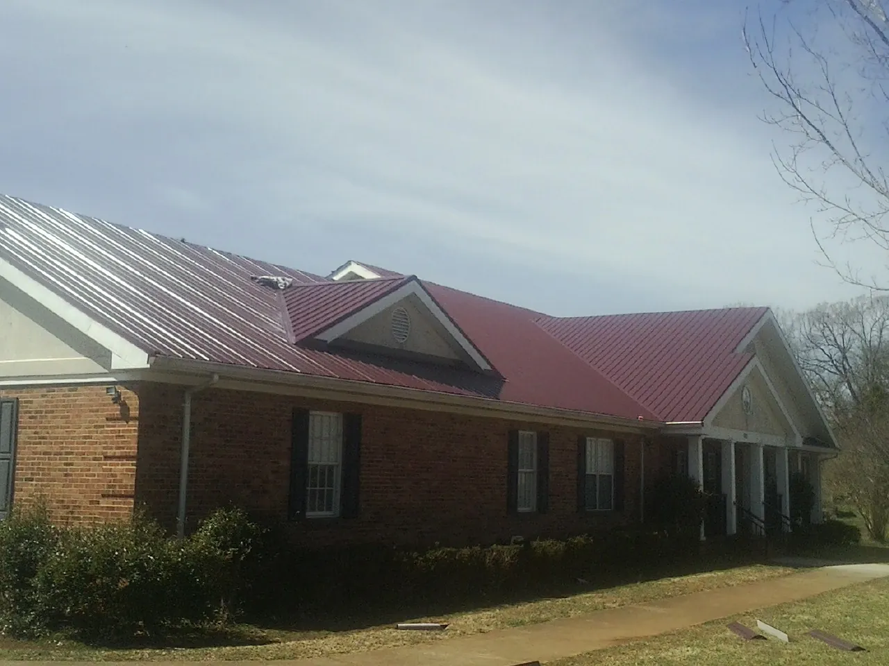Red metal roof with gabled entries on a long brick building, from a Hail Damage Roof Repair job in Bon Aqua
