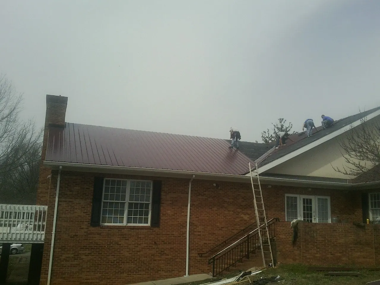 Crew setting red metal roofing panels on a brick home in Bon Aqua