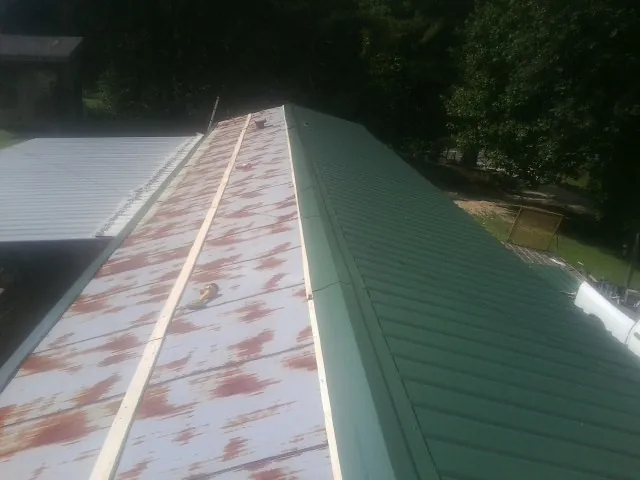 Old rusted panels beside newly installed green metal roofing — Wind Damage Roof Repair by Roofing Brothers in Bon Aqua