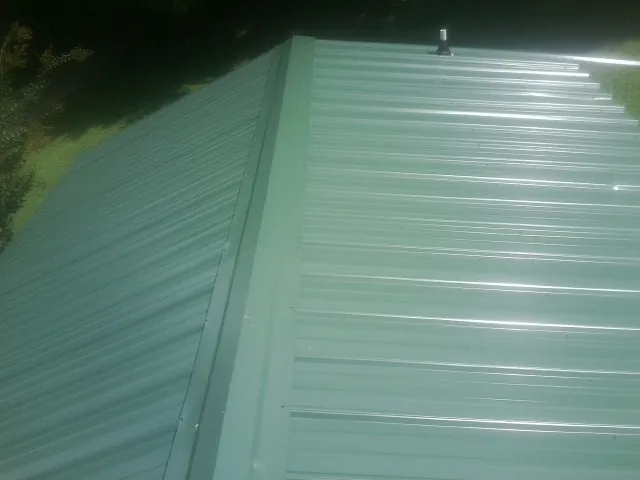 New green metal panels meeting at the ridge of a roof — Flat Roof Repair work by our crew in Bon Aqua