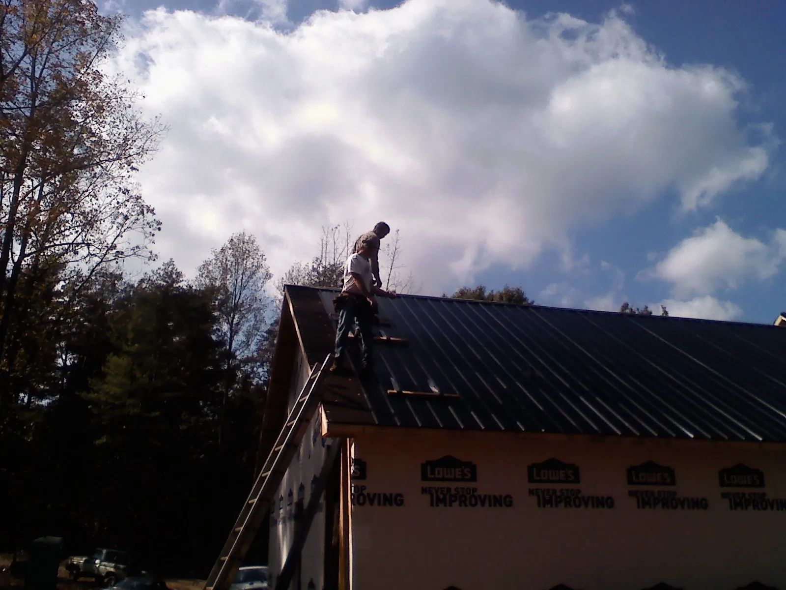 Roofer fastening dark metal panels high against a cloudy sky, from a Roof Inspection job in Bon Aqua