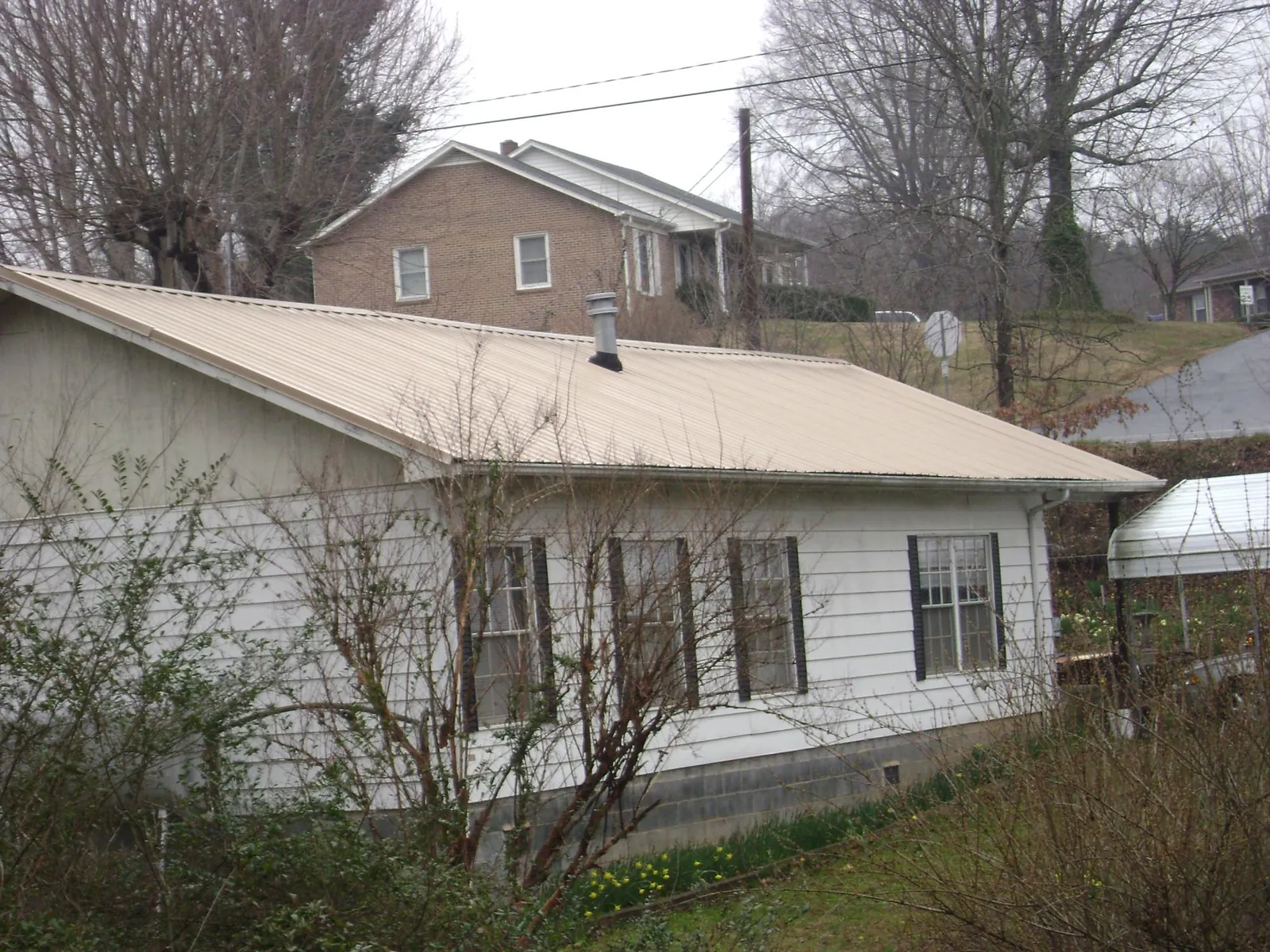 Tan metal roof on a white sided house set into a hillside — Commercial Roofing by Roofing Brothers in Bon Aqua