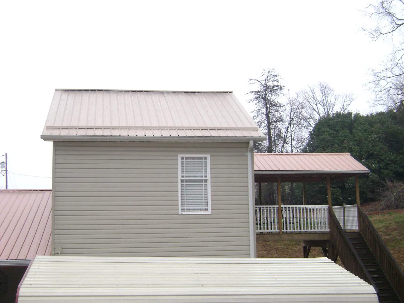 Tan metal roofs on a two story addition and attached porch, from a Roof Replacement job in Bon Aqua